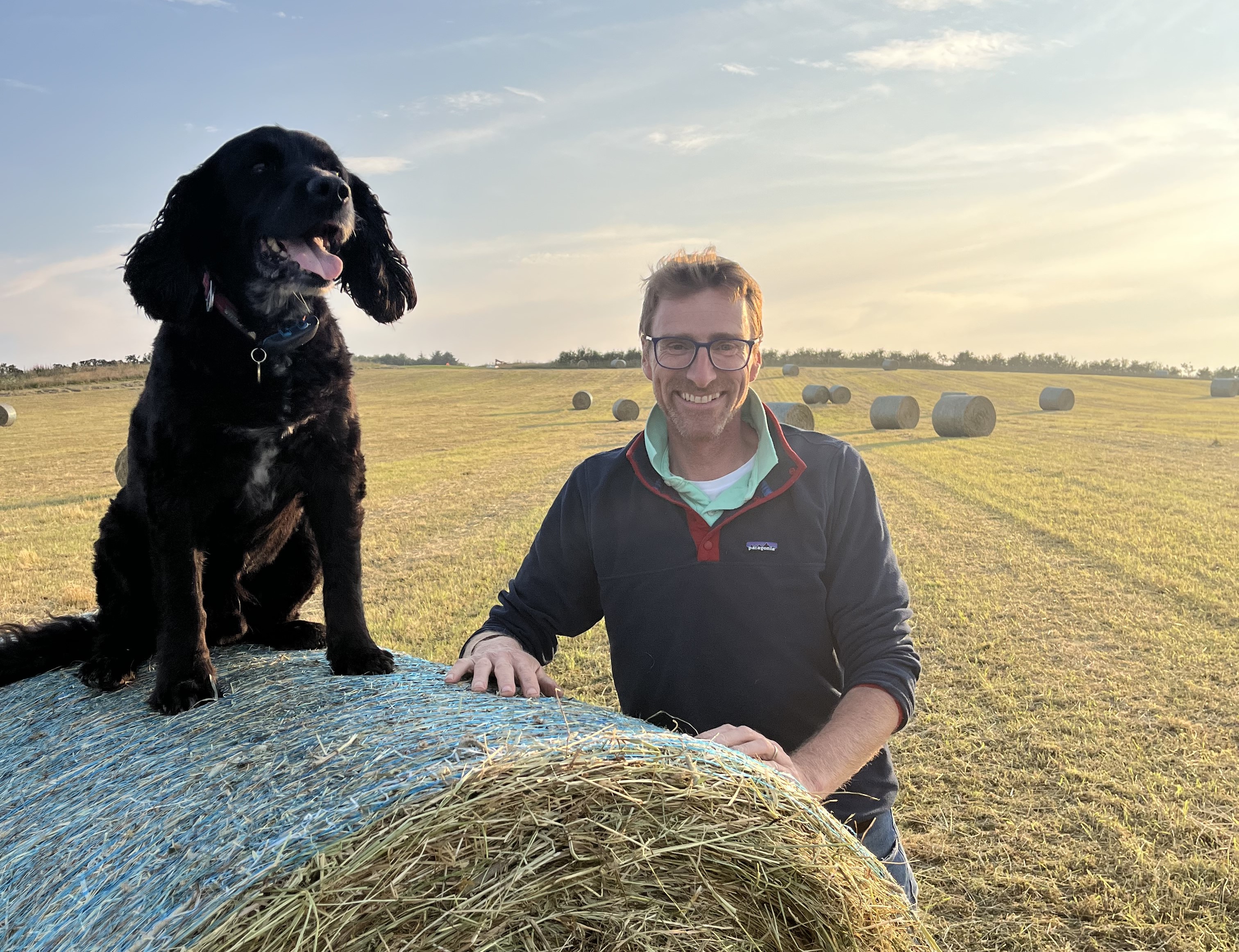 Richard Lockett with a dog on a hay bale at Knockbain Farm